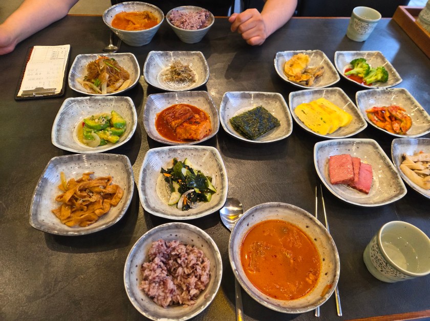 Traditional Korean side dish spread Multiple small dishes of Korean side dishes including kimchi, vegetables, seaweed, egg, and tofu with bowls of rice and soup